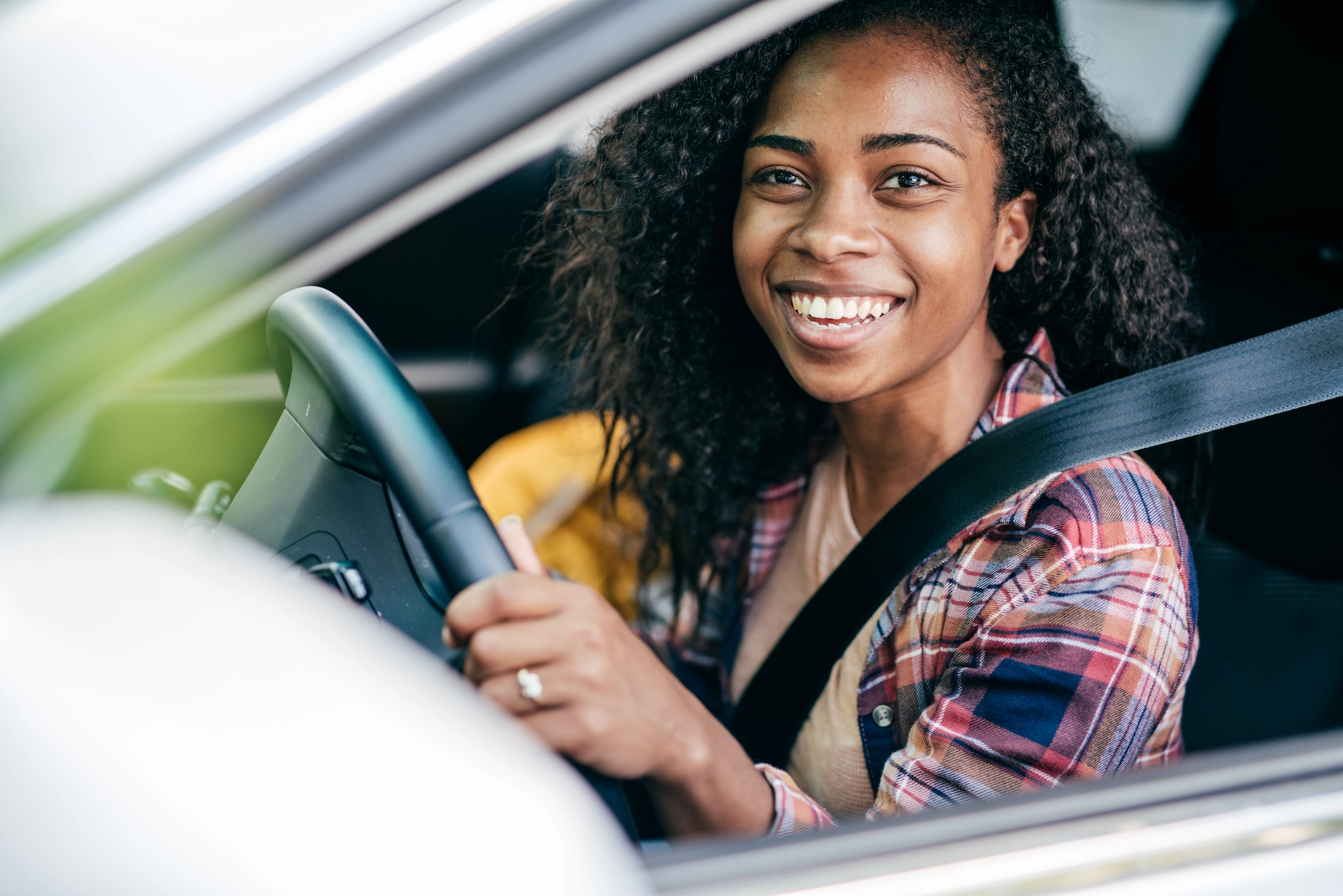 Woman smiling in the driver's seat of a car, buckled up with hands on the steering wheel